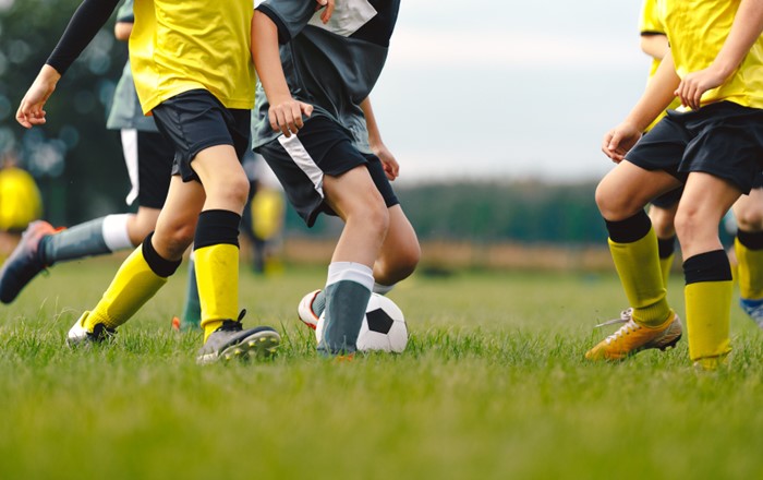 Youngsters pictured from chest down playing football on an outdoor pitch