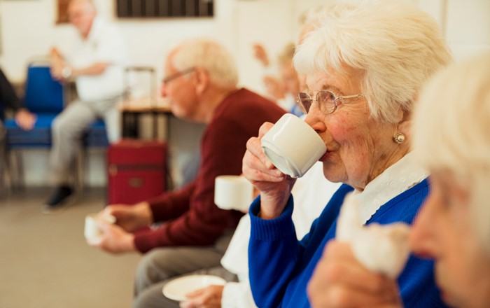 A close up shot of an elderly woman drinking tea with friends.