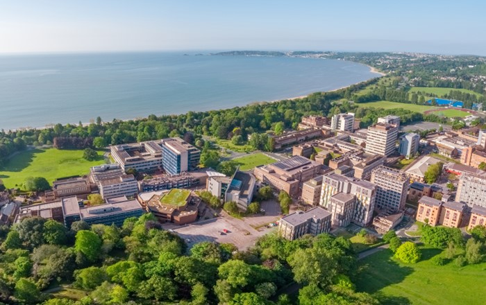 Aerial photograph of a group of buildings surrounded by parkland with the sea in the background