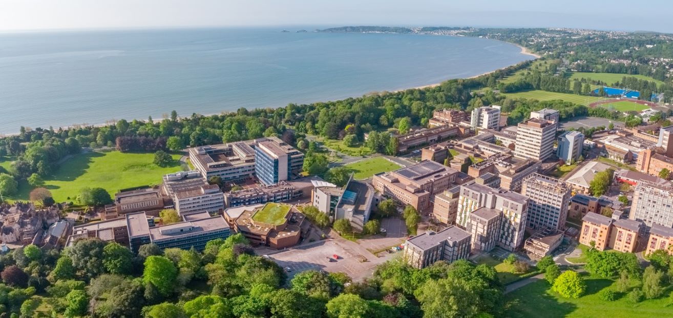 Aerial photograph of a group of buildings surrounded by parkland with the sea in the background