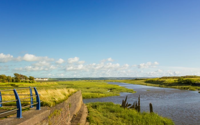 View across an estuary surrounded by marshes with a wall and railings