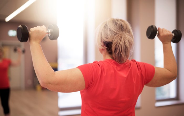 Woman with her back to the camera lifting two hand weights 