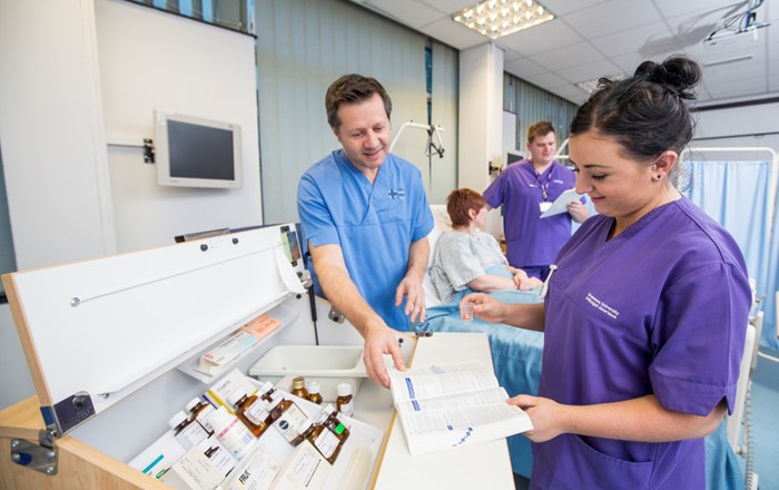 Nurses in uniform on a ward looking at charts by a drugs cabinet