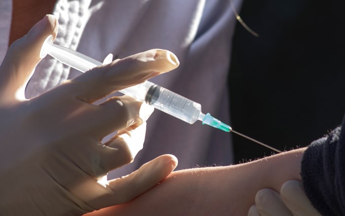 Close-up image of hand holding a syringe injecting someone in the arm