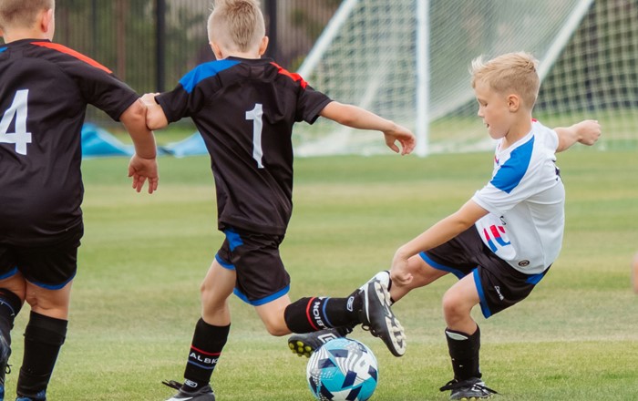 Two young boys in kit playing football on an outdoor pitch