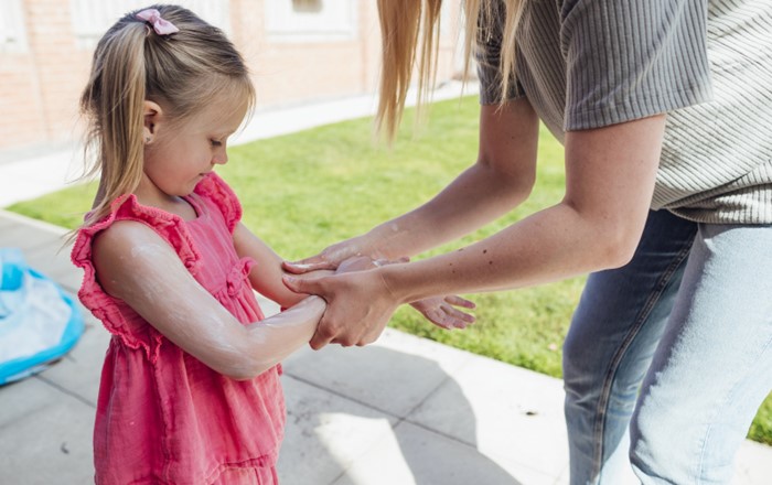 Adult woman standing in a garden applying suncream to a small girl's arms