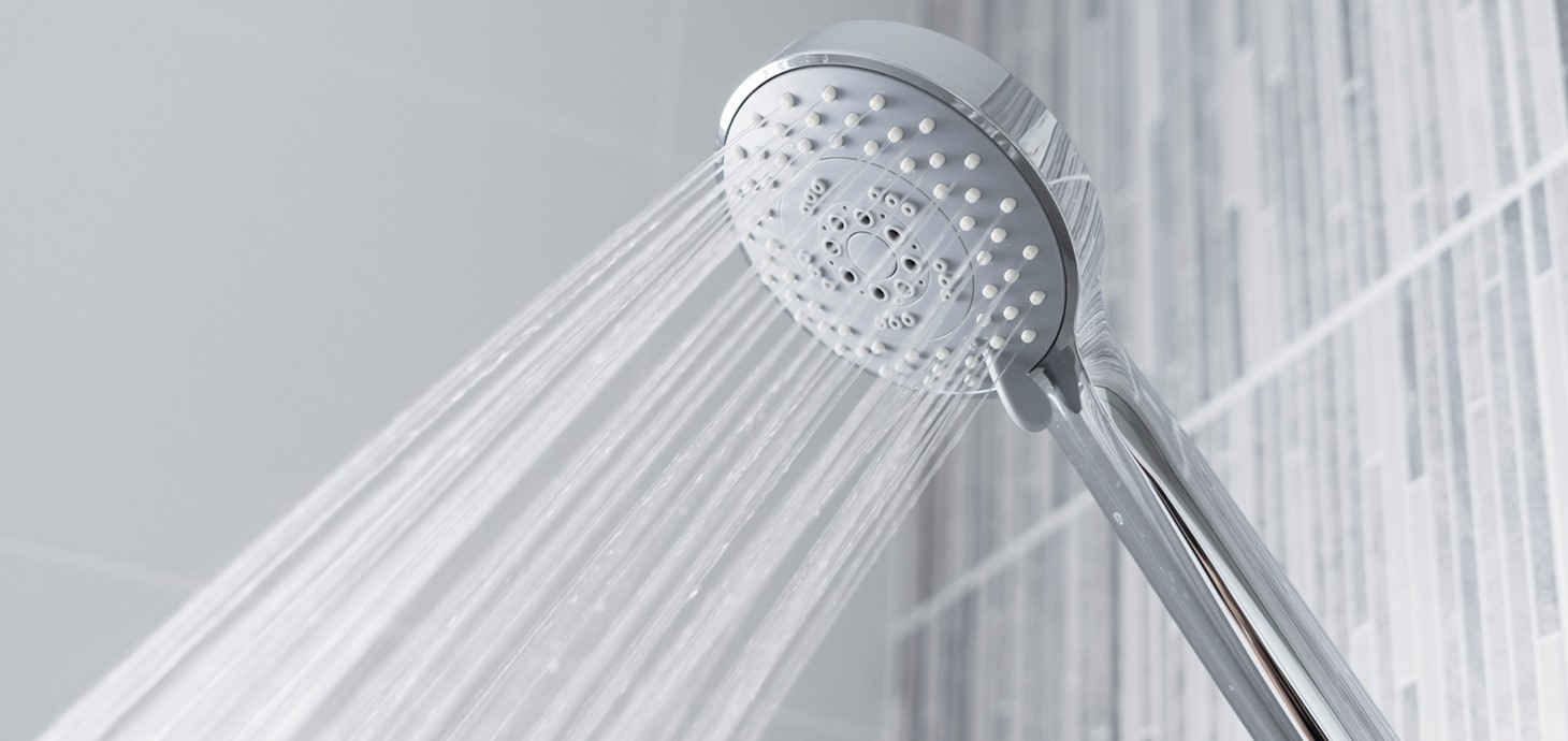 Water pouring out of a metallic shower head attached to a tiled wall