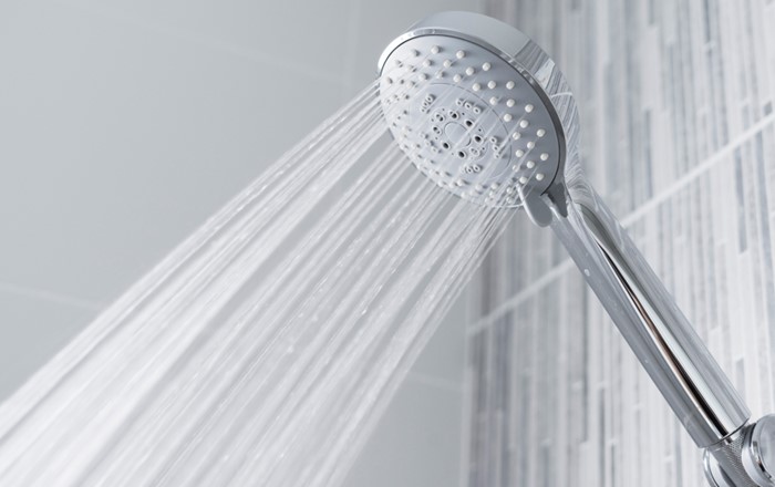 Water pouring out of a metallic shower head attached to a tiled wall