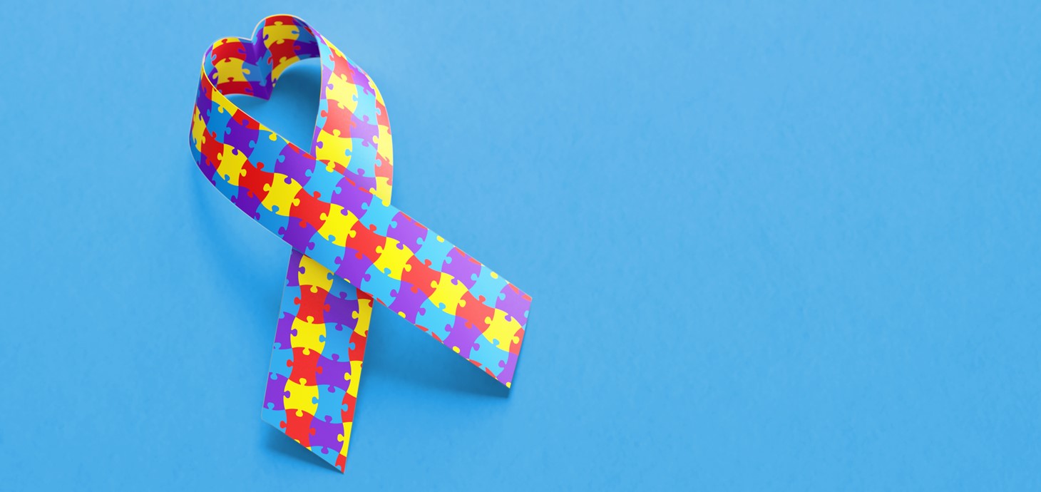 Ribbon featuring jigsaw pieces denoting autism awareness on a plain blue background