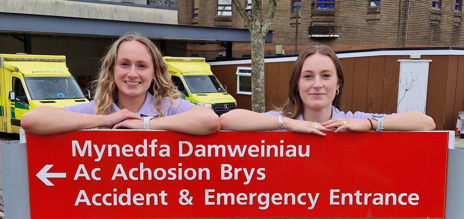 Two young women standing outside a building leaning over a sign