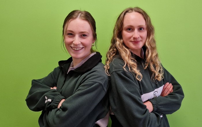 Two young women standing back to back with their arms folded