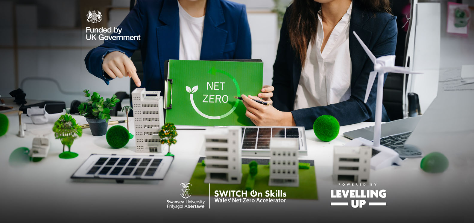 A green sign with the words ‘net zero’ is held above a white and green scale model of an industrial park.