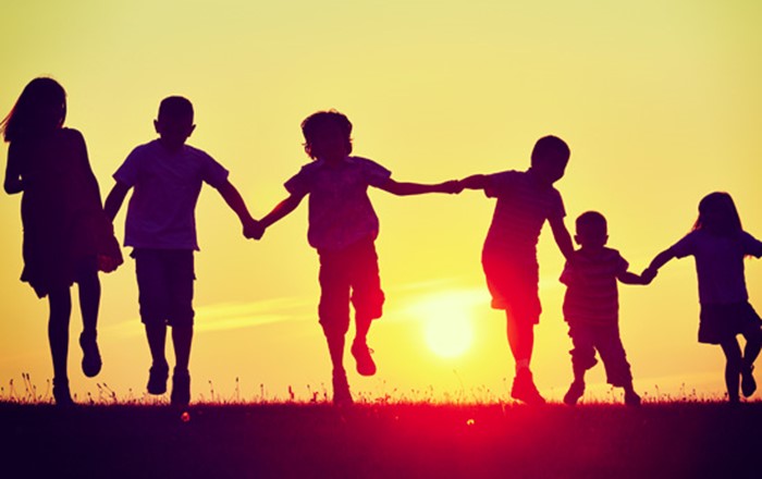 Silhouette of six people of various ages holding hands outside with sunset in background