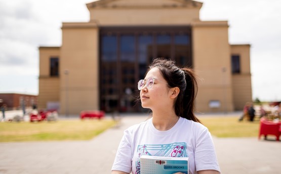 women standing with books. framed by building behind her