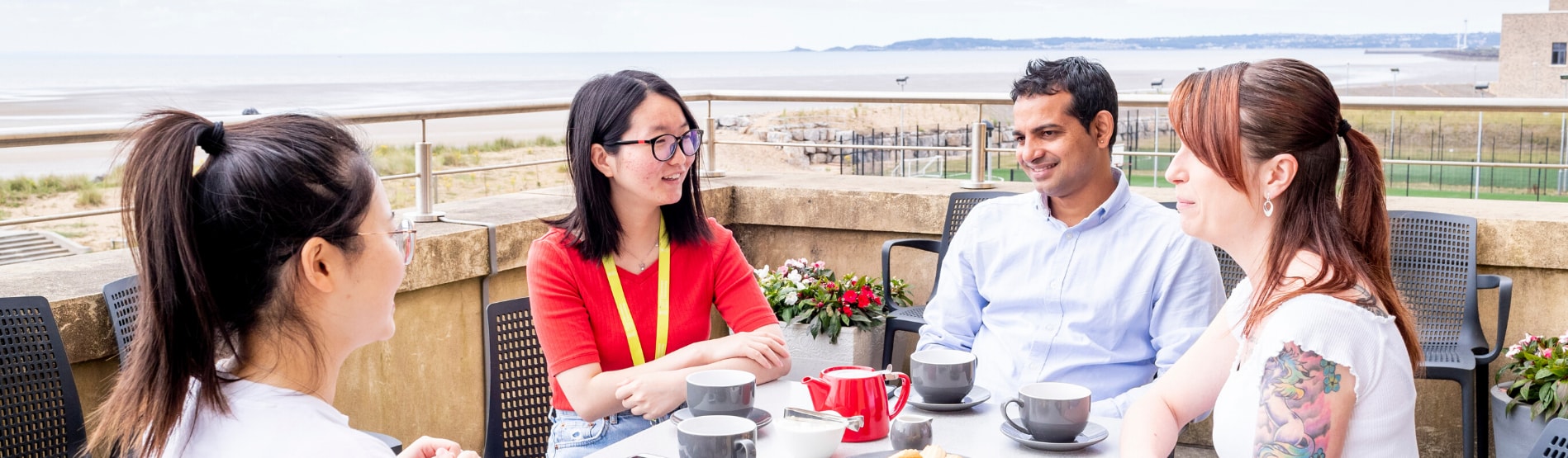 Group of postgraduate researchers drinking coffee and sitting outside in Bay Campus