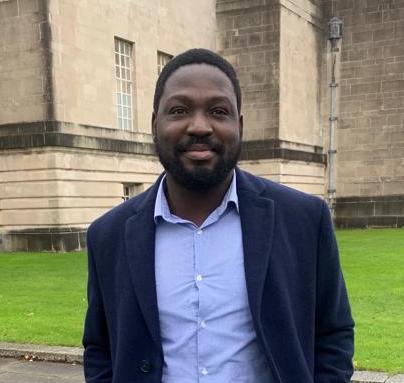 Kwabena standing in front of a wall in a suit