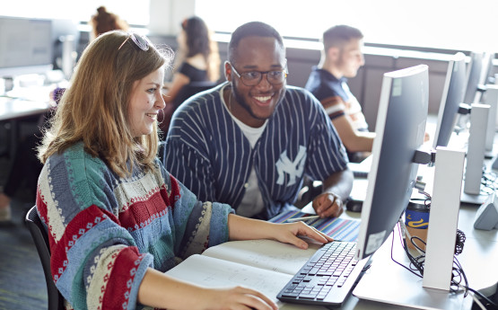 Students sat working at a computer and smiling 