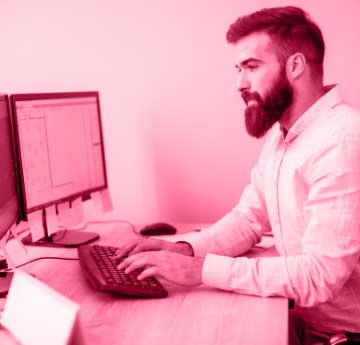 A young man with beard working on his computer at his desk