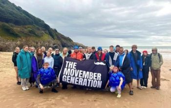 Students holding Movember flag after doing a Movember Charity sea dip on the beach. 