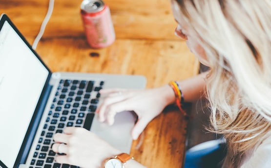 Image of a students hands typing on laptop with a soft drink can in background