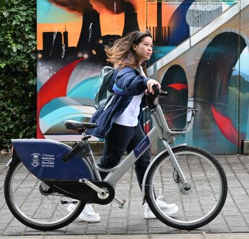 Cyclist walking past art mural on Singleton Campus