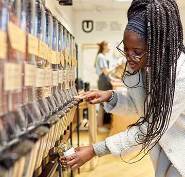 An image of a female student filling a container in Root Zero zero waste shop on Singleton Campus, Swansea University. 