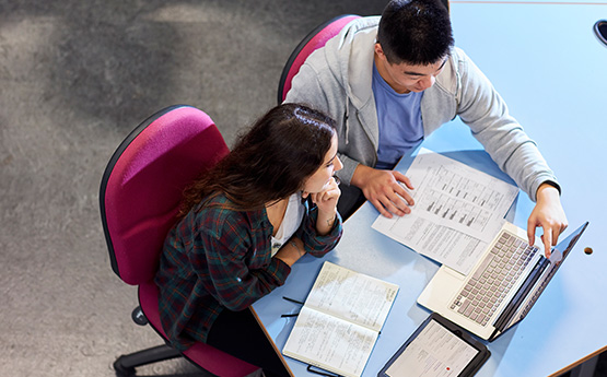 Students studying with laptops and papers on table.