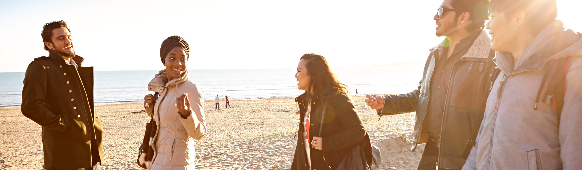 Students walking along Swansea beach in the sun.