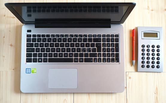 Image of a laptop computer, a calculator and a pen looking over from above.