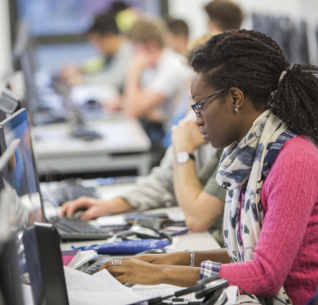 Female student sat at a computer in a busy library