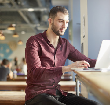 Male student sitting in a café looking at his laptop screen